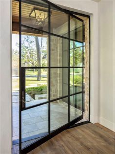 an open glass door leading to a patio area with wood floors and white walls, in front of a brick wall