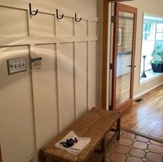 a wooden bench sitting in front of a white wall with hooks on it's sides