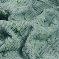 a green knitted blanket with holes in the middle and two rows of buttons on it