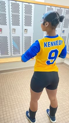 a woman in a yellow and blue uniform standing on a tile floor next to lockers