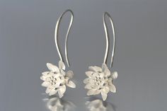 Silver Earrings - Delicate waterlilies are fixed on a gracefully-curved silver wire that forms into a silver ear wire.  Originally crafted from a single sheet of metal, they have been cast and finished with a satin texture. <br><br>Available in two sizes and three finishes: bright sterling silver, oxidized sterling silver, and 18k gold.<br><br>Small size hangs 1.33L and .6W, large hangs 1.25L and .75W.<br><br>Please make your selections below. Venue Aesthetic, Modern Hoop Earrings, Silversmithing Jewelry, Silver Gold Earrings, Ladies Dress Watches, Desi Wedding Dresses, Book Crafts Diy, Pendant Sets, Metalwork Jewelry