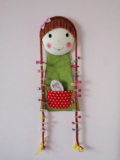 the doll is hanging on the wall with her hair tied in pigtails and wearing a green dress