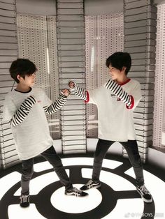 two young men standing on top of a circular object in front of a wall with blinds