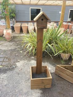 a wooden birdhouse sitting on top of a planter next to potted plants