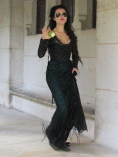 a woman in a long black dress holding an apple and making the peace sign with her hand