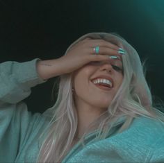 a woman smiling and holding her hands up to her face while wearing a hoodie