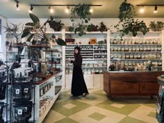 a woman standing in the middle of a store with lots of plants and bottles on shelves