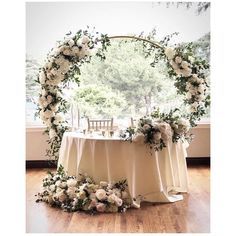 a table with white flowers and greenery on it in front of a large window