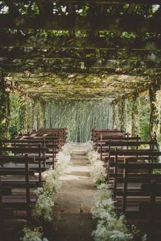 an outdoor wedding ceremony with wooden pews and white flowers on the aisle, surrounded by greenery