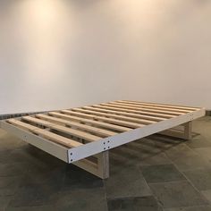 a wooden bed frame sitting on top of a stone floor next to a white wall