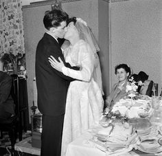 a bride and groom kissing in front of their wedding cake at the table with guests