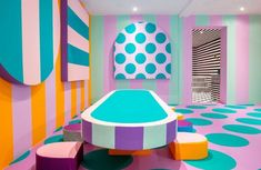 a brightly colored room with an oval shaped table and stools in the center, surrounded by polka dot wallpaper