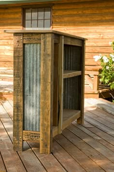 an old wooden cabinet sitting on top of a wooden deck next to a building with a green roof