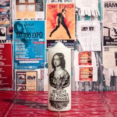 a candle sitting on top of a red table covered in posters and flyers with the words, believe all things are possible