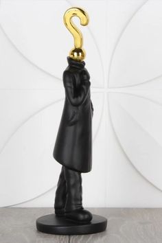 A sleek black statue of a person with a gold question mark for a head stands on a round base. The figure wears a long coat, creating a mysterious tone.