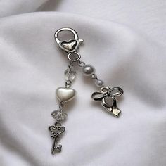 a key chain with two charms attached to it on a white fabric background that has hearts and keys hanging from it