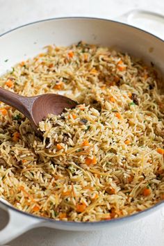 a pot filled with rice and carrots on top of a table next to a wooden spoon