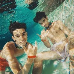 two young men swimming in a pool making the peace sign