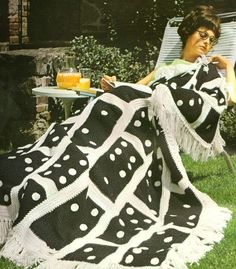 a woman sitting in a chair on the grass with a black and white blanket draped over her