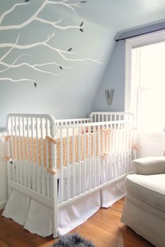 a baby's room with a white crib and tree decal on the wall