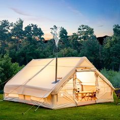 a tent set up in the middle of a field with trees and grass around it