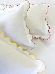 two white scalloped pillows with pink trim on them sitting on a white surface