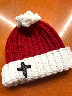 a red and white knitted hat with a black cross on the front sitting on a wooden table