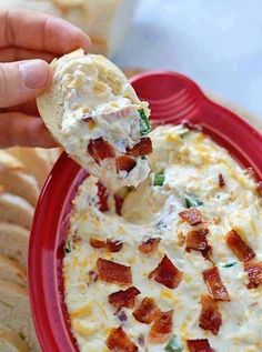 a red bowl filled with dip and bacon on top of crackers next to bread