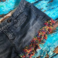 an old pair of jeans with colorful fringes on them sitting on a wooden surface