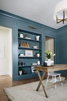 a dining room with blue walls and white chairs in front of a wooden table surrounded by bookshelves