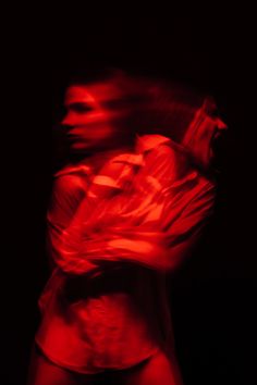 a blurry image of a woman in red light with her arms crossed and hands behind her back