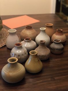 many different colored vases sitting on a wooden table with an orange piece of paper in the background