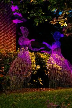 two purple sculptures in front of a brick building with trees and bushes around them at night