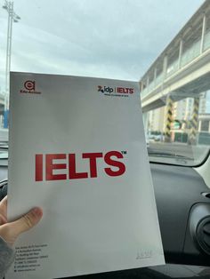 a hand holding up a paper with the word ielts on it in front of a car