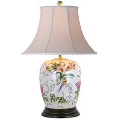 a white lamp with flowers on it and a bird design on the bottom, sitting next to a beige shade