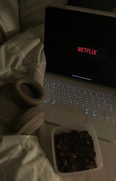 a laptop computer sitting on top of a bed next to a bowl of chocolate chips