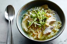 a bowl of soup with noodles, chicken and broccoli in it next to a spoon