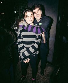 two people standing next to each other in a room with dark walls and flooring