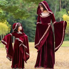 a woman and child dressed up in medieval costumes, standing in a field with trees behind them