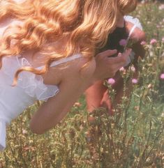 a woman in a white dress taking a photo with her cell phone while standing in a field