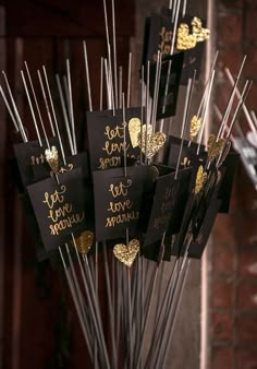 there are many black and gold tags hanging from the top of some sticks with hearts on them