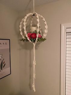 a hanging candle holder with roses and greenery in the center, on a wall