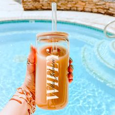 a person holding up a drink in front of a swimming pool