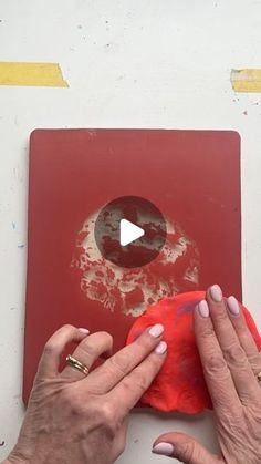 two hands are using a red cloth to clean a piece of artwork on a white surface