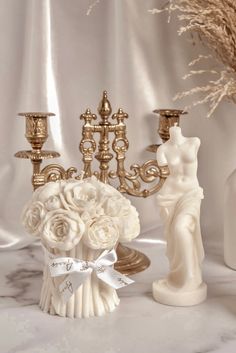 two vases with flowers and candles are sitting on a marble countertop next to gold candelabras