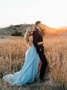 a man and woman are standing in the middle of a field with tall grass at sunset