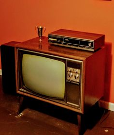 an old fashioned tv sitting on top of a wooden stand in front of a red wall