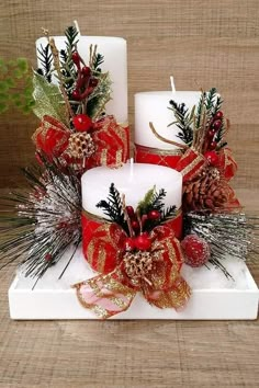 two white candles decorated with red and gold ribbons, pine cones, and evergreens