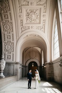 a bride and groom are standing in an ornate building with large windows on the ceiling