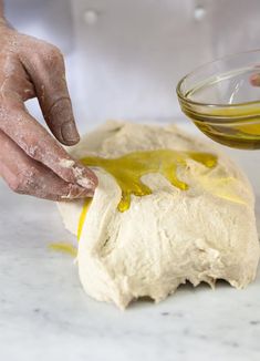 a person is kneading dough into a bowl with olive oil on the side